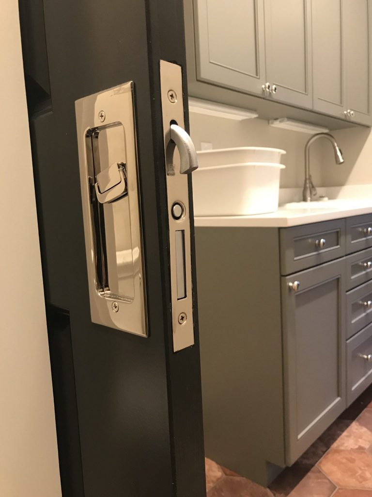 A partially open door reveals a laundry room with a sink, white basin, and gray cabinets. The door has a metal latch handle.